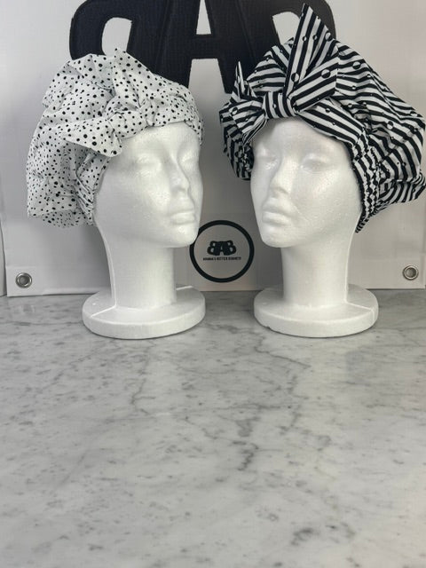 Two shower caps on small styrofoam mannequin heads โ polka dot and striped styles โ showing fit on approximately 21-23 inch head circumference